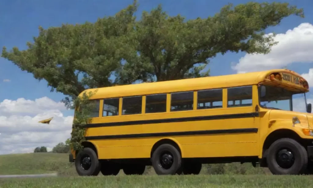 El autobús amarillo da vuelta hacia un árbol verde con hojas de aviones