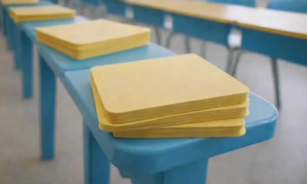 Los colores cálidos amarillos resaltan perfiles de estudiantes diversos en mesas azules ya desgastadas